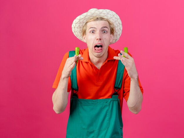 Hombre joven jardinero vestido con mono y sombrero sosteniendo mitades de ají verde