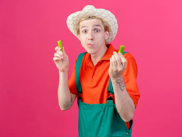 Hombre joven jardinero vestido con mono y sombrero sosteniendo mitades de ají verde