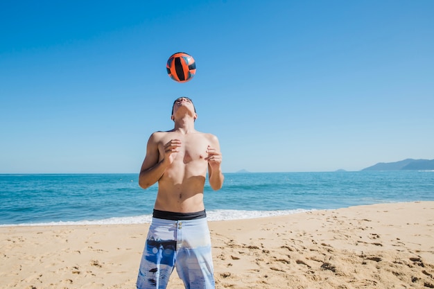 Hombre joven jugando al fútbol en la playa soleada