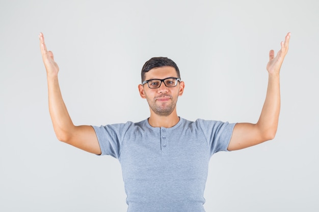 Foto gratuita hombre joven levantando los brazos y sonriendo en camiseta gris, vista frontal de gafas.