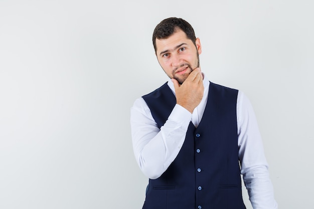 Hombre joven con la mano en la barbilla en camisa, chaleco y elegante