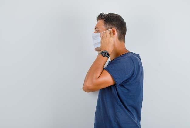 Hombre joven con máscara médica en camiseta azul oscuro.