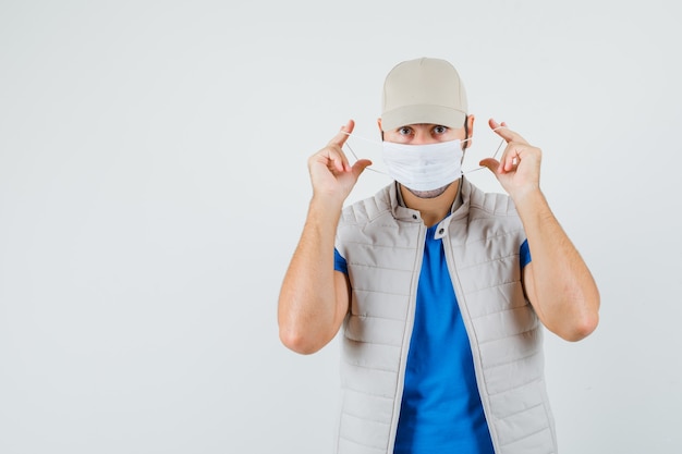 Hombre joven con máscara médica en camiseta, chaqueta y mirando con cuidado. vista frontal.