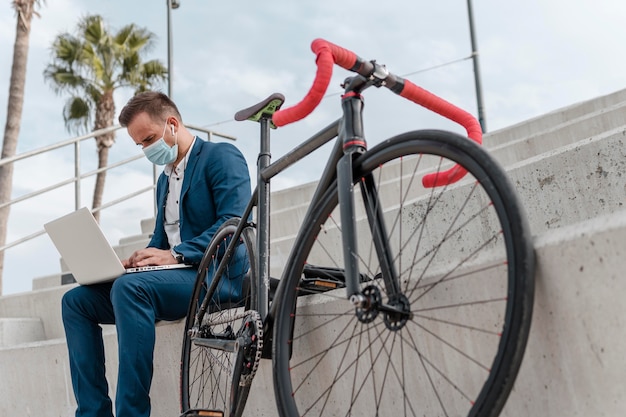 Hombre joven con una máscara médica mientras está sentado junto a su bicicleta