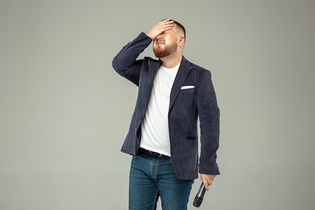 Hombre joven con micrófono en estudio gris, concepto líder.