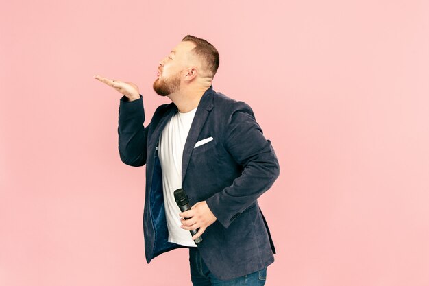 Hombre joven con micrófono en rosa, con micrófono en concepto de estudio.