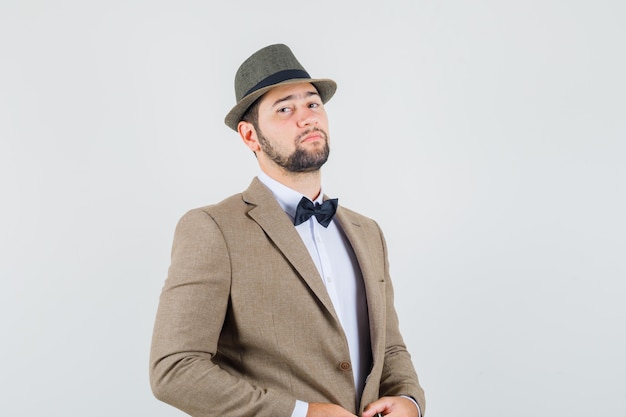Hombre joven mirando a la cámara en traje, sombrero y mirando confiado, vista frontal.