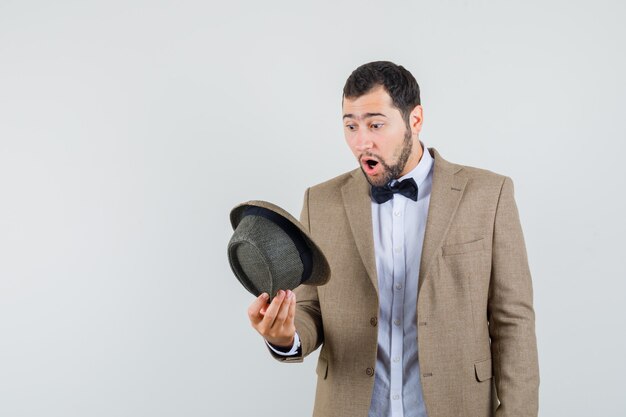 Hombre joven mirando con sombrero en traje y mirando asombrado, vista frontal.