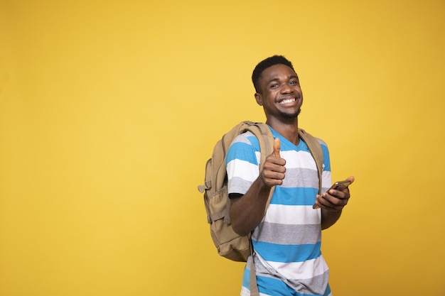 Hombre joven con una mochila haciendo el gesto de pulgar hacia arriba mientras usa su teléfono