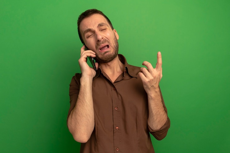 Foto gratuito hombre joven molesto hablando por teléfono apuntando hacia arriba con los ojos cerrados aislado en la pared verde