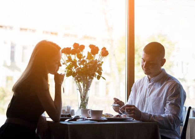 Hombre joven y mujer atractiva en la mesa con postres y flores
