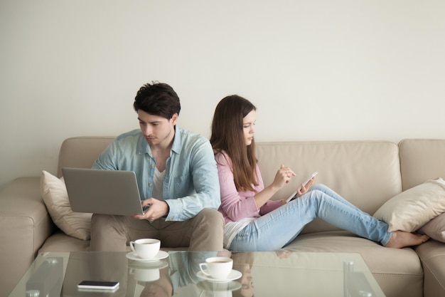 Hombre joven y mujer espalda con espalda usando laptop