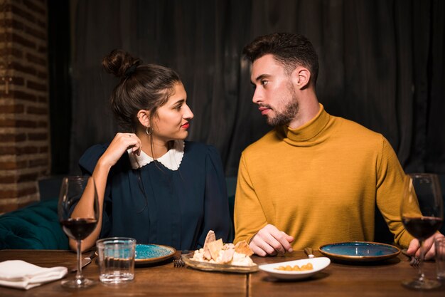 Hombre joven y mujer en la mesa con copas de vino y comida en el restaurante