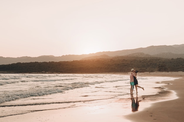 Hombre joven y mujer que se besan en la playa en la puesta del sol.