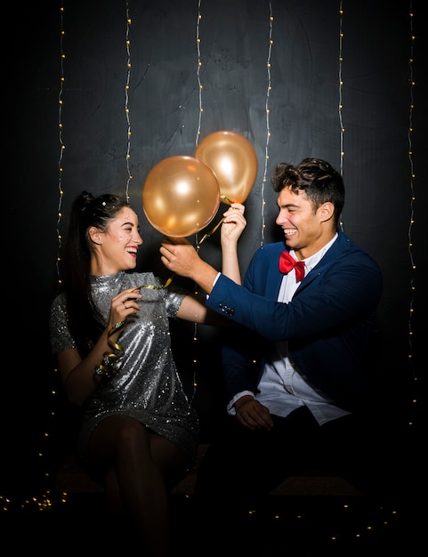 Hombre joven y mujer sonrientes con los globos en banco