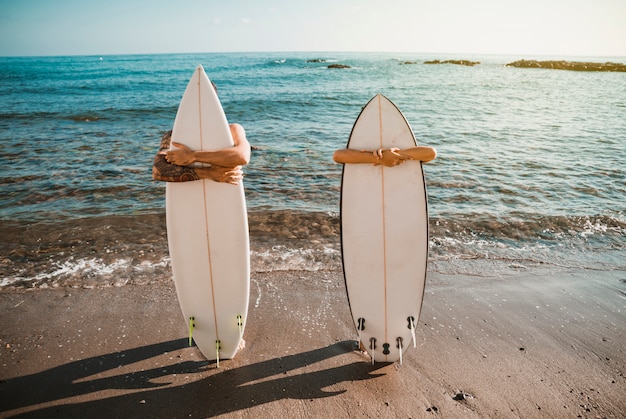 Hombre joven y mujer con tablas de surf en la costa cerca del agua