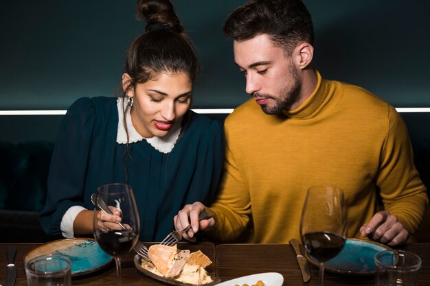 Hombre joven y mujer con tenedores en la mesa con copas de vino y comida en el restaurante