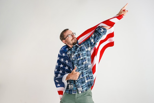 Foto gratuita hombre joven orgulloso que sostiene la bandera de los estados unidos de américa aislado en el estudio blanco.