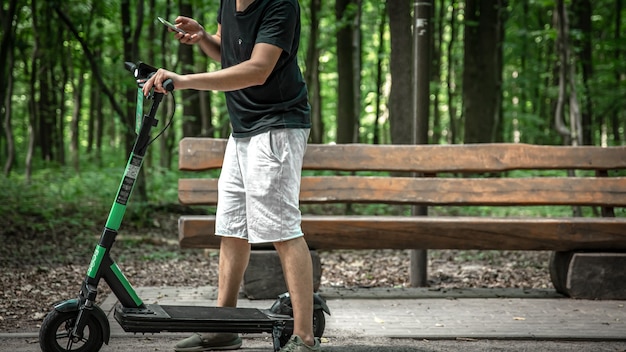 Hombre joven en un parque de la ciudad con un scooter eléctrico.