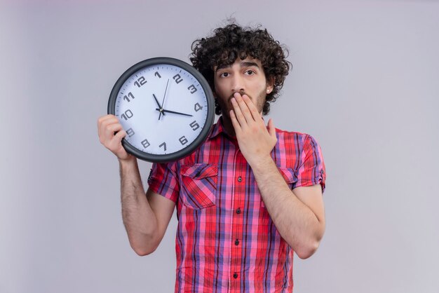Hombre joven de pelo rizado aislado camisa colorida con reloj sorprendido