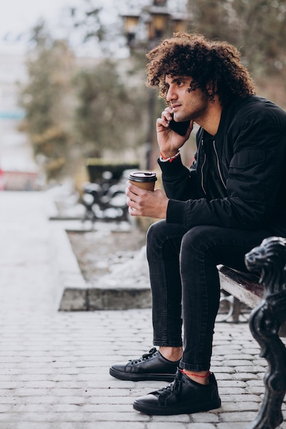 Hombre joven con pelo rizado tomando café y hablando por teléfono