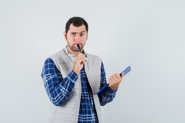 Hombre joven pensando en algo para escribir en camisa, chaqueta y mirando con cuidado, vista frontal.