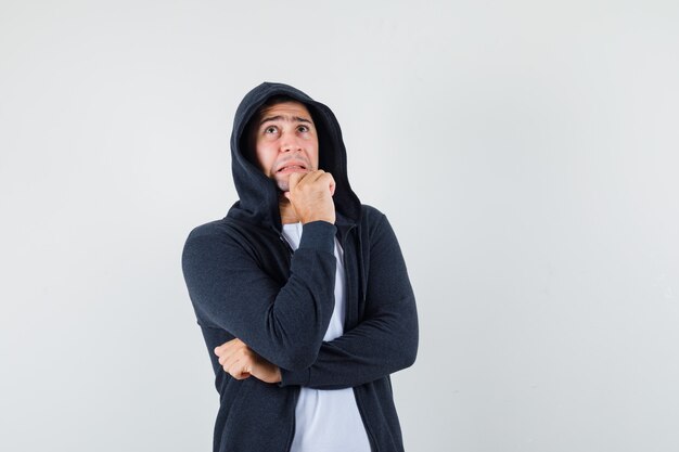 Hombre joven pensando en camiseta, chaqueta y mirando preocupado, vista frontal.