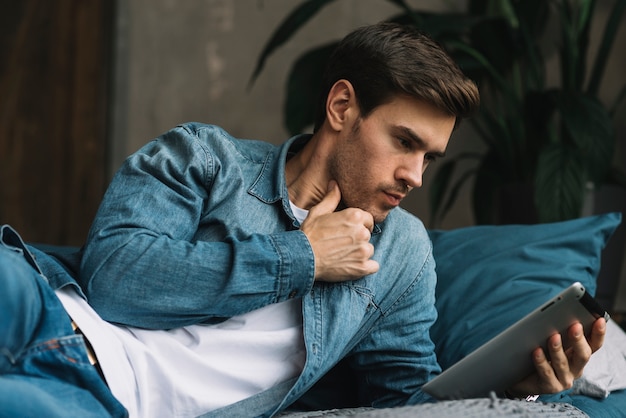 Foto gratuita hombre joven pensativo que mira la tableta digital