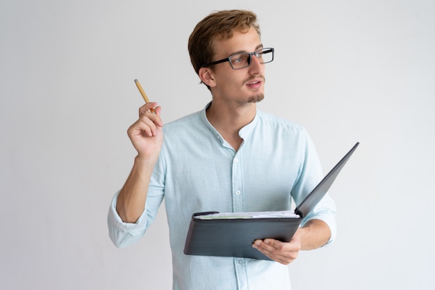 Hombre joven pensativo que sostiene el archivo, pluma y tener idea