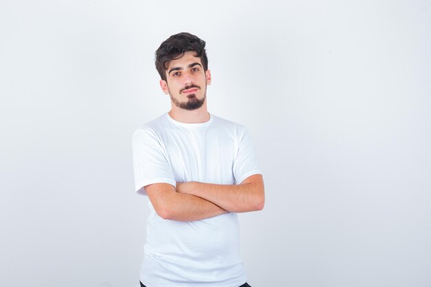 Hombre joven de pie con los brazos cruzados en camiseta y mirando confiado