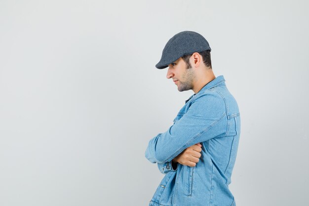 Hombre joven de pie con los brazos cruzados en chaqueta, gorra y mirando tranquilo. . espacio para texto