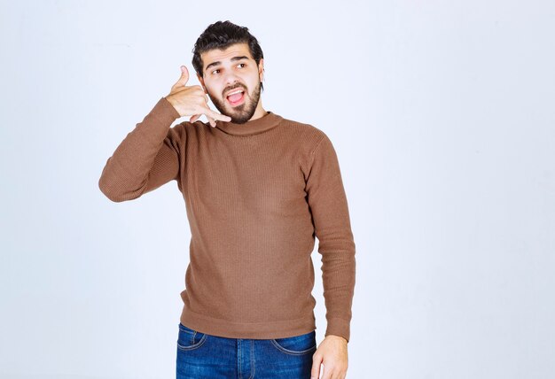 Hombre joven de pie levantando sus dos dedos como apoderarse del teléfono aislado sobre un fondo blanco. Foto de alta calidad