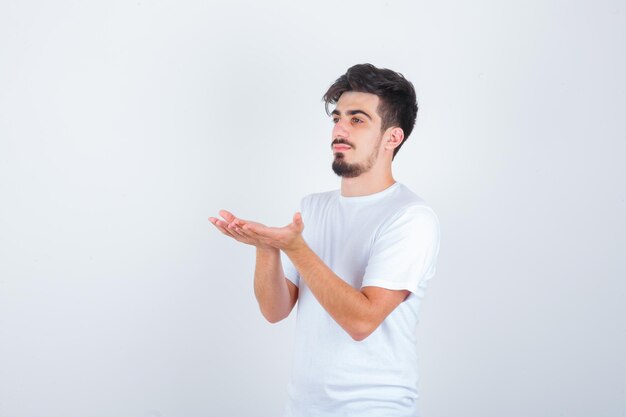 Hombre joven de pie con las manos ahuecadas en camiseta blanca y mirando confiado