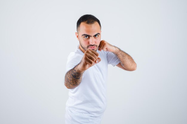 Hombre joven de pie en pose de boxeador en camiseta blanca y mirando serio