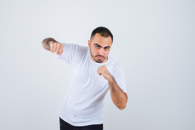 Hombre joven de pie en pose de boxeador en camiseta blanca y mirando serio