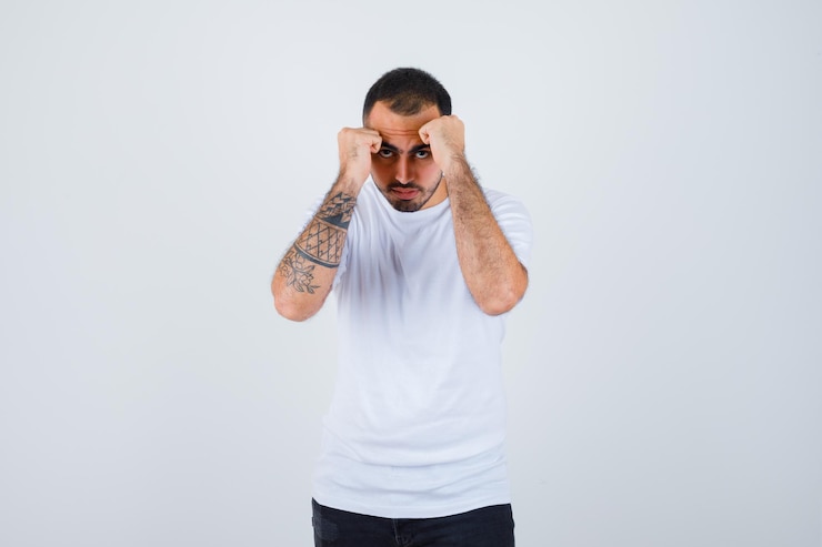 Foto gratuito hombre joven de pie en pose de boxeador en camiseta blanca y mirando serio