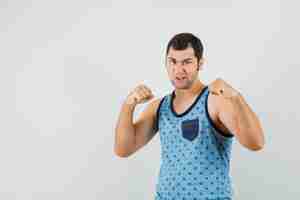 Foto gratuita hombre joven de pie en pose de lucha en camiseta azul y mirando furioso, vista frontal.