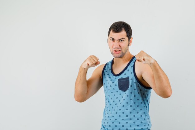 Hombre joven de pie en pose de lucha en camiseta azul y mirando furioso, vista frontal.