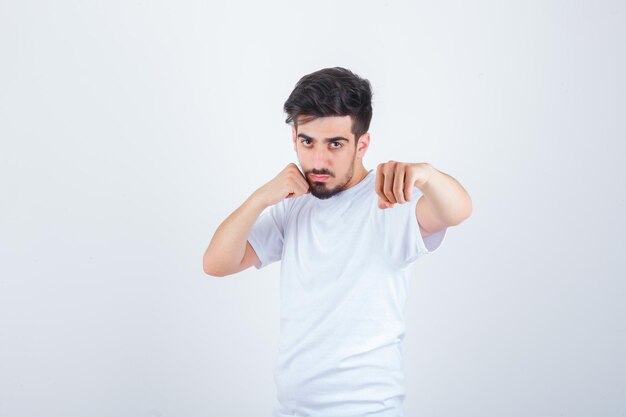 Hombre joven de pie en pose de lucha en camiseta blanca y mirando confiado