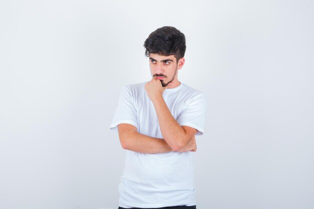 Hombre joven de pie en pose de pensamiento mientras mira a otro lado en camiseta y mirando pensativo