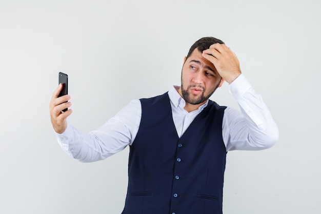 Hombre joven posando mientras toma selfie en camisa y chaleco y se ve guapo