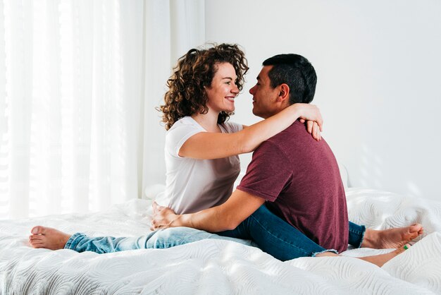 Hombre joven que abraza a la mujer feliz en cama