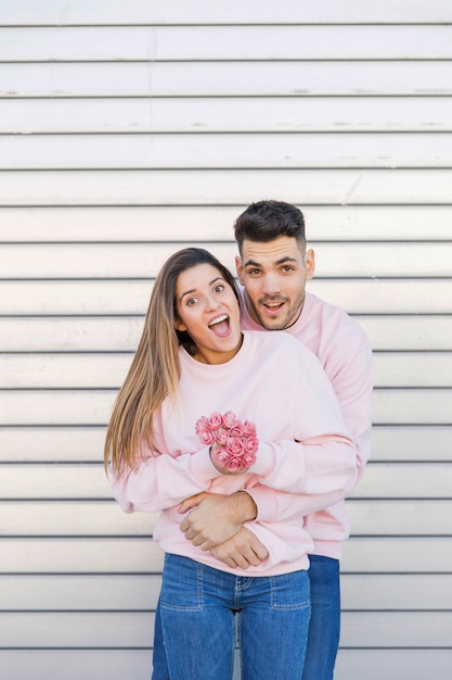 Hombre joven que abraza a la mujer sorprendida atractiva con las flores