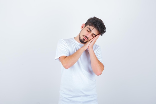 Hombre joven que se acurruca la cara en sus manos en camiseta y parece soñoliento