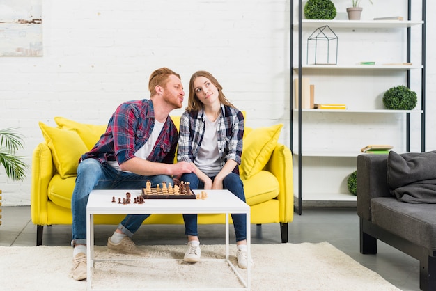 Foto gratuita hombre joven que ama a su novia que se sienta en el sofá amarillo que juega a ajedrez en casa