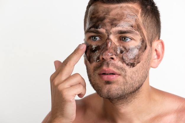 Hombre joven que aplica la máscara negra en su cara contra el fondo blanco