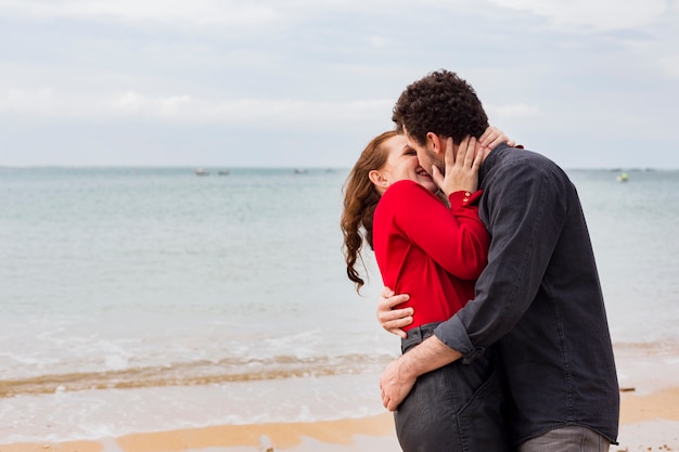 Hombre joven que besa a la mujer en orilla de mar
