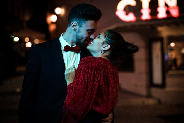Hombre joven que besa y que abraza a la mujer feliz atractiva encantadora en la calle