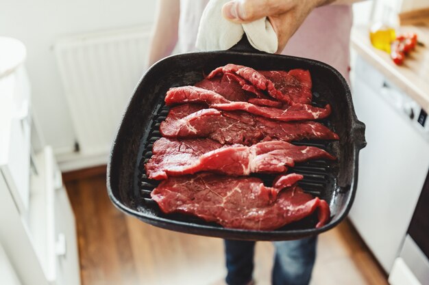 Hombre joven que cocina la carne cruda en la cacerola de la parrilla