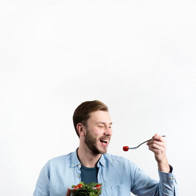 Foto gratuita hombre joven que come el tomate y la ensalada rojos de cereza en el fondo blanco